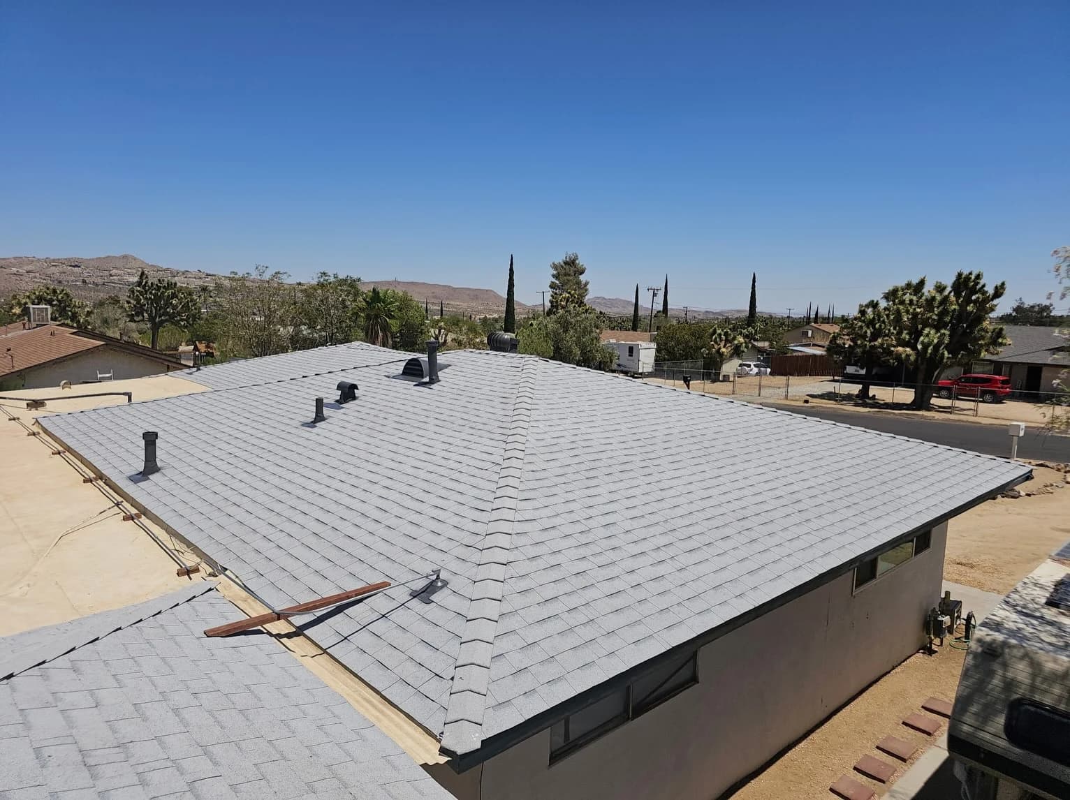 Gray shingles and hip caps around several roof vents and pipe penetrations