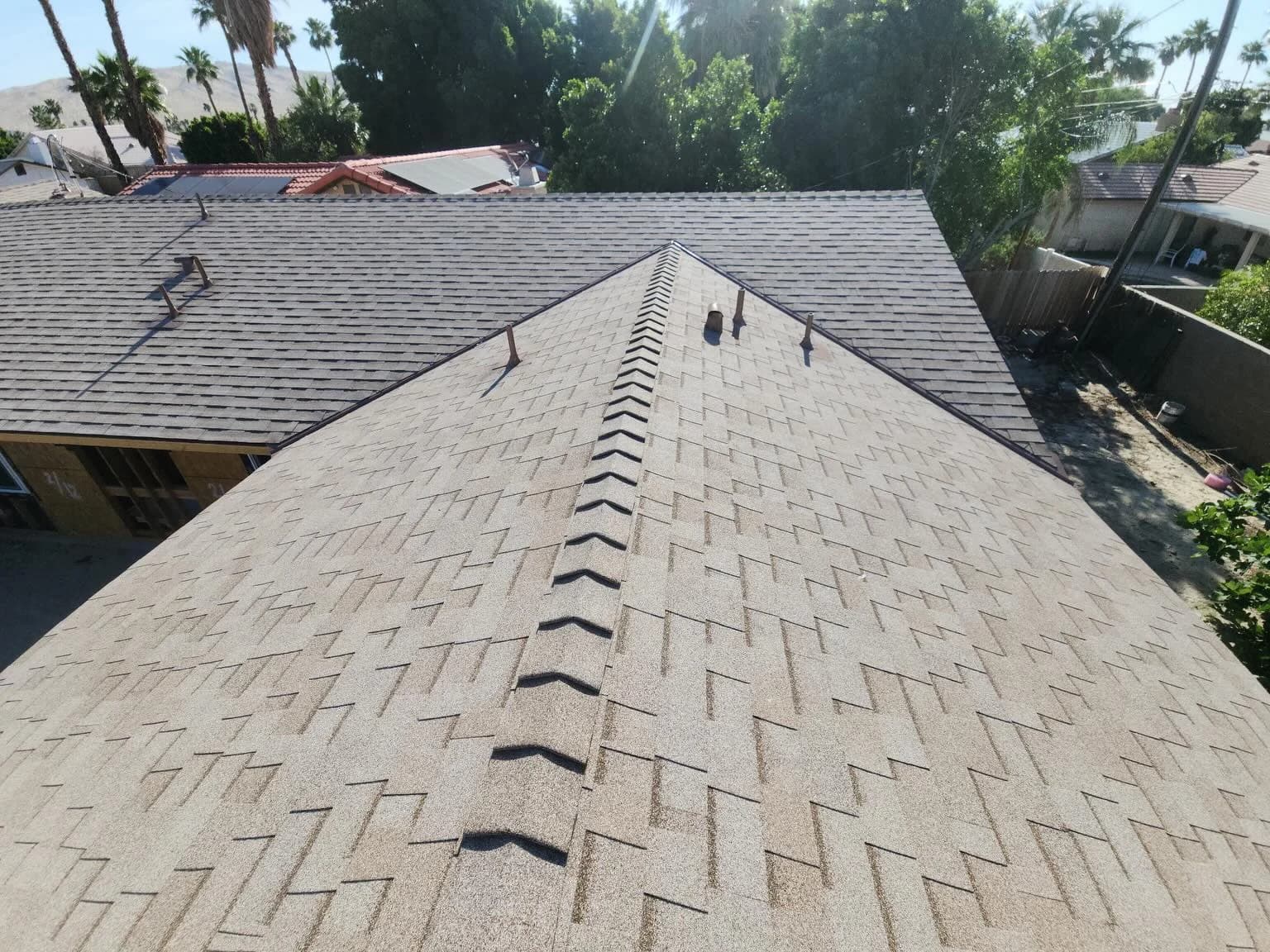 Gray shingles on intersecting gable roofs with ridge caps and vent pipes